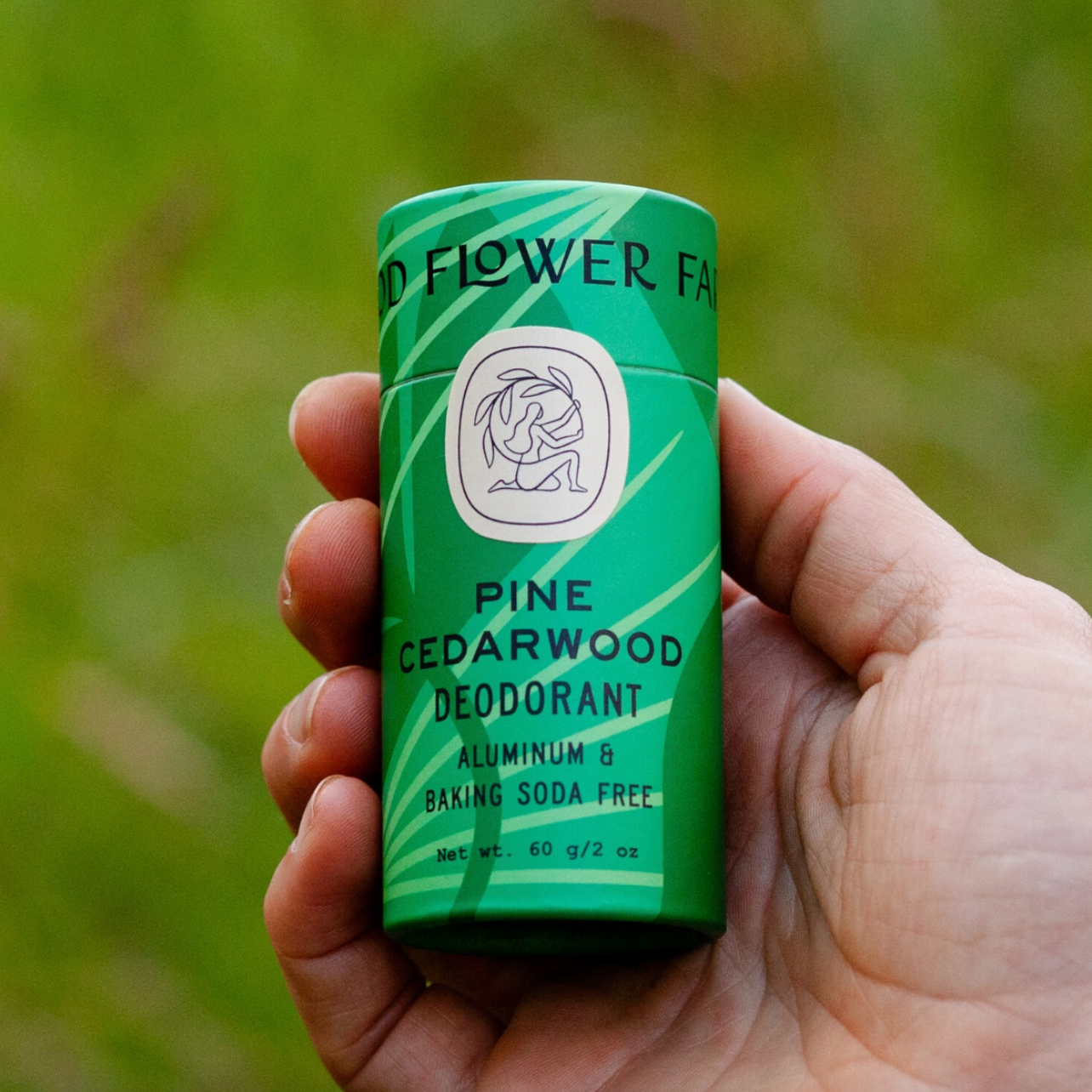 hand holding green paper tube of pine cedarwood deodorant in park 