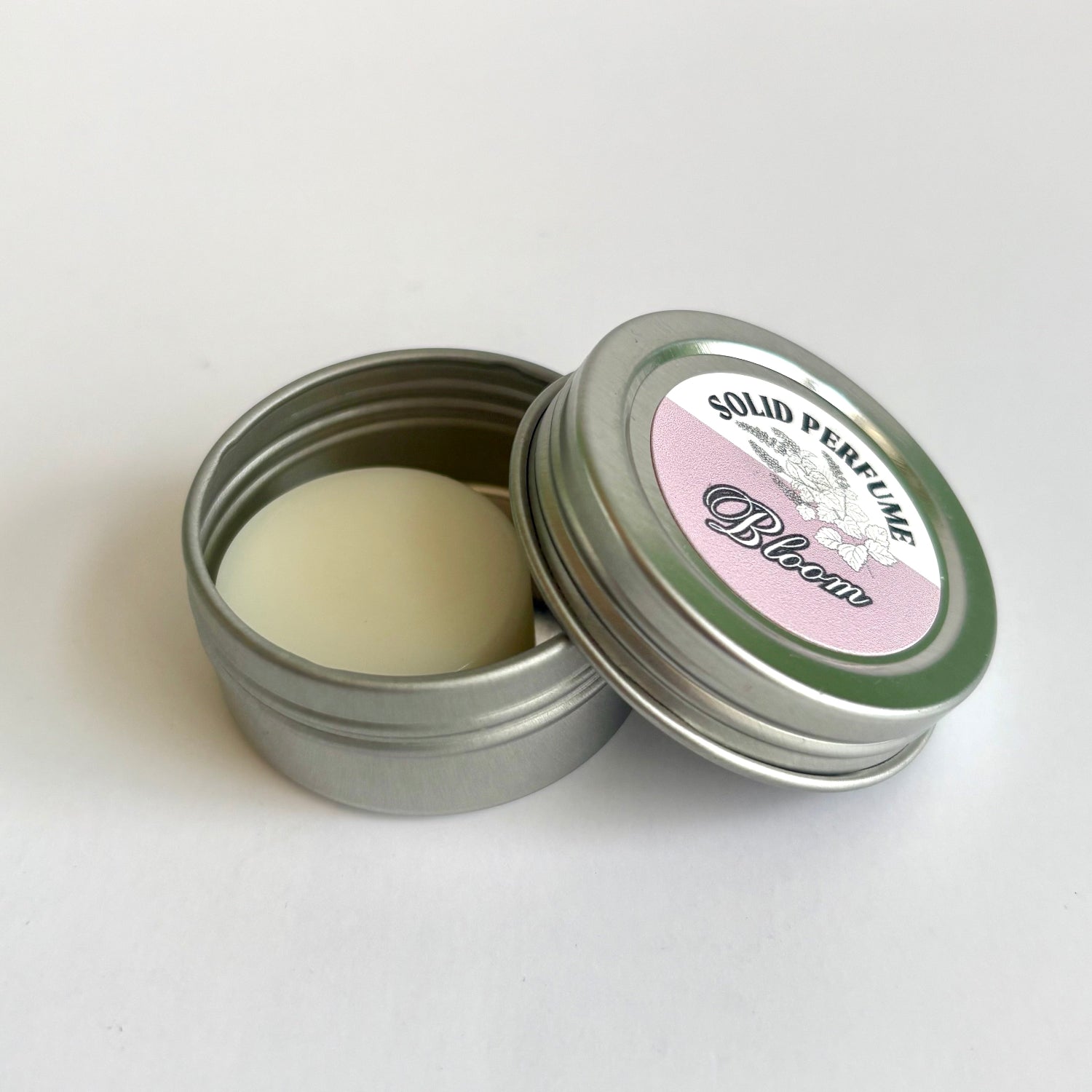 Solid perfume in a metal tin with a decorative label on a white background