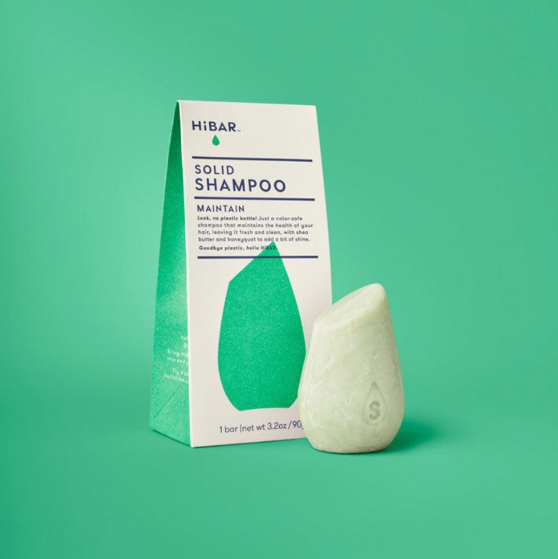 Solid shampoo bar and packaging on a green background