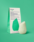 Solid shampoo bar and packaging on a green background