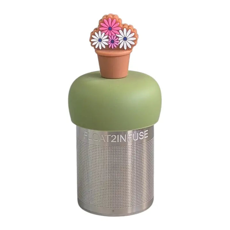 The Teany Tiny Kitchen Floating Tea Infuser features a stainless steel design with a green silicone lid topped by a brown flower pot with pink and white flowers, making tea steeping fun and enjoyable.