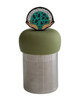 The Teany Tiny Kitchen Floating Tea Infuser features a stainless steel design with a green silicone lid topped by a hands holding a circle full of trees and seeds arcing between the hands is text reading "there is no Planet B"
