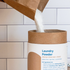 cardboard tube being filled with laundry powder from paper bag on white tile background