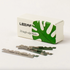 A Leaf Razor Blades box, featuring a green leaf design and the Leaf brand, sits next to three recyclable stainless steel blades for your safety razor on a white surface.