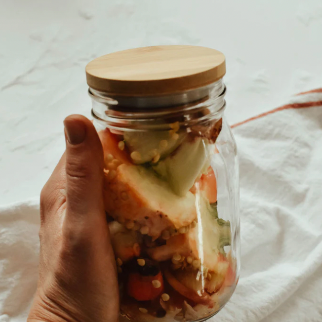 A hand holding a mason jar full of food scraps with a bamboo lid. 