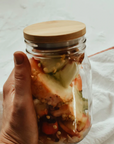 A hand holding a mason jar full of food scraps with a bamboo lid. 