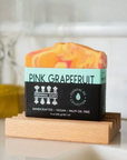 A vibrant bar of Perennial Soaps Bar Soaps, handcrafted in Wisconsin with orange and pink swirls and a turquoise label, highlights its vegan and palm oil free features. A blurred yellow soap sits in the background.