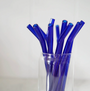 A clear glass displays several upright Mermaid Straw Glass Bent Straws against a plain, light-colored background.